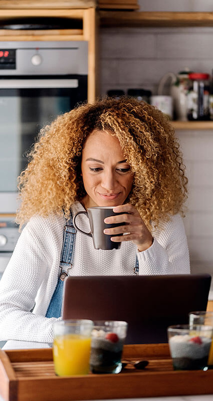Ein Frau mit Kaffeetasse sucht in ihrem Laptop nach günstigen Darlehen.